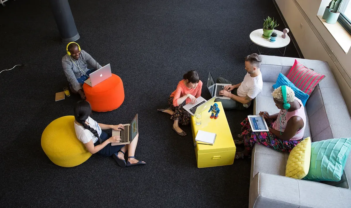 Team collaborating on laptops in a colourful lounge, like the Voxly Vision enterprise sales team