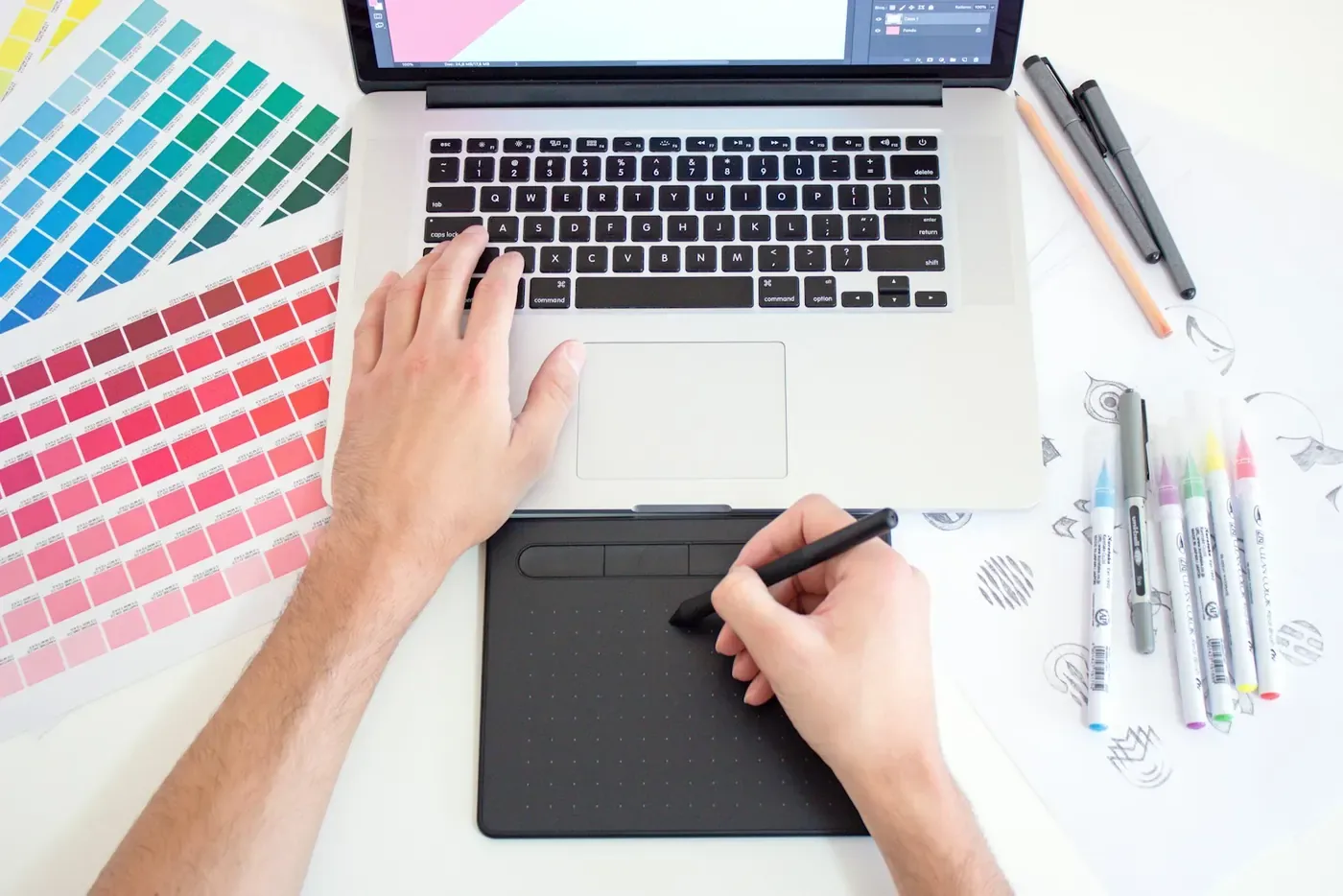 Designer working on a laptop with colour swatches, uploading ad creative to the Voxly Vision web app for a compliance check