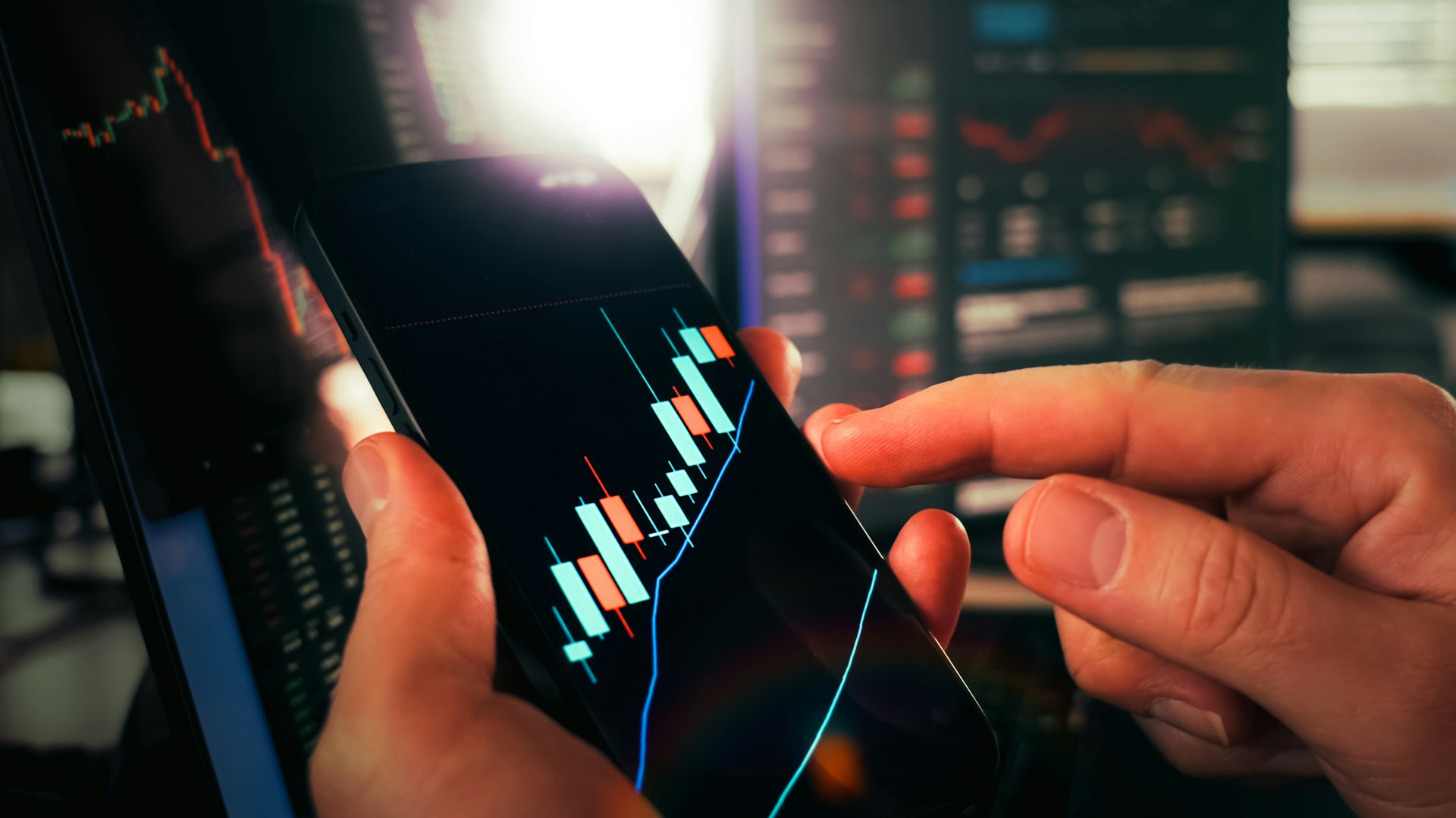 Close-up of hands using a trading app on a smartphone, with a candlestick price chart on screen