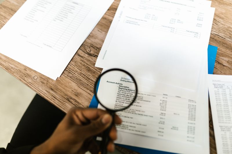Hand holding a magnifying glass over a document to check the small print