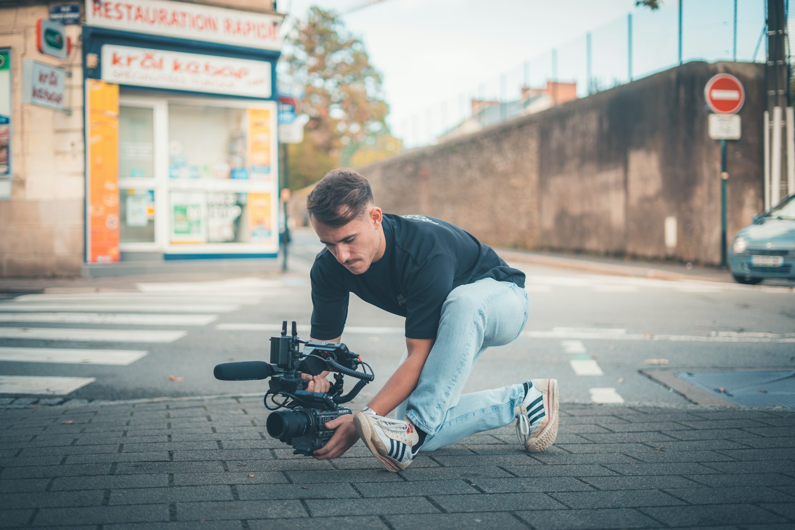 Videographer crouching on a city street to film social content, the kind of creative agencies check with Voxly Vision before it goes to the client. Photo by Gabriel Weyand on Unsplash